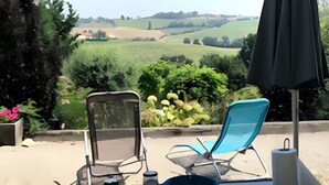 Une table dressée à l’extérieur, avec vue sur des collines verdoyantes, deux chaises et une table sur laquelle sont disposées des assiettes, des bols et des tasses.