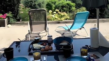 A table set outdoors with a view of rolling hills, two chairs, and a table with plates, bowls, and cups.