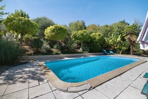 En rektangulær swimmingpool med en klar, blå vandoverflade, omgivet af en flisbelagt terrasse.