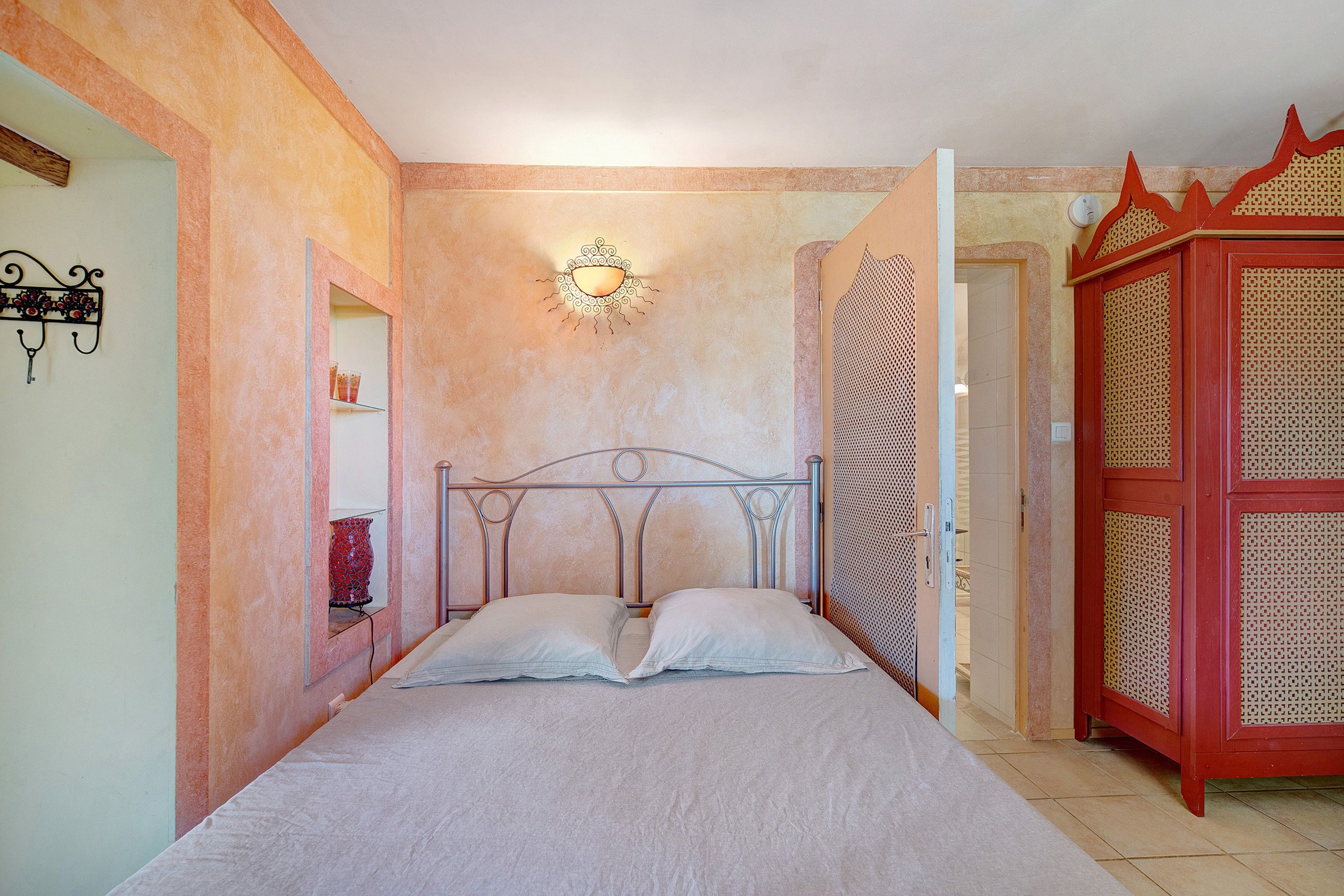 Une chambre à coucher avec un lit, un luminaire fixé au mur et une armoire rouge.