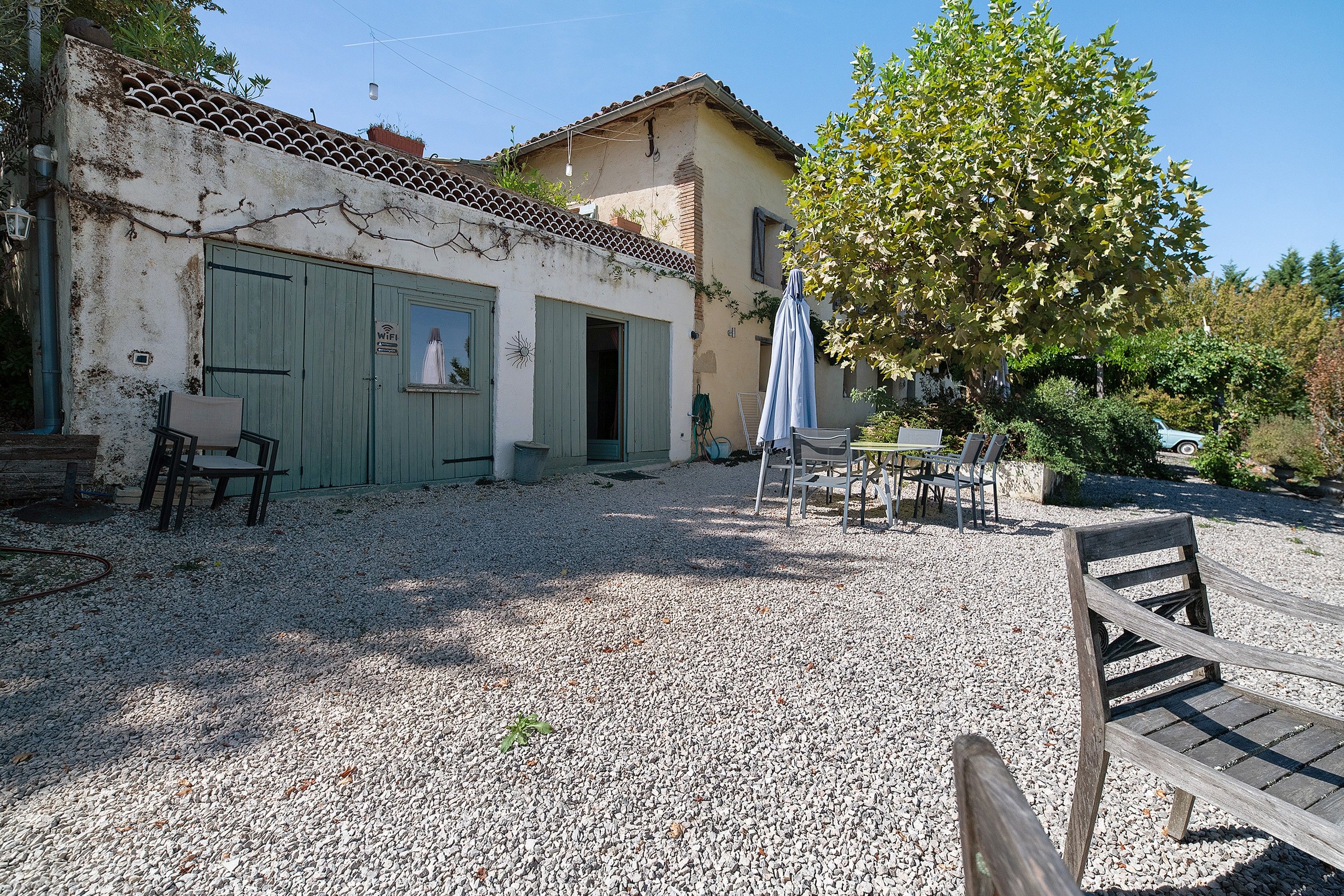 Un bâtiment doté d’un toit en tuiles, d’une cour en gravier et de mobilier d’extérieur.