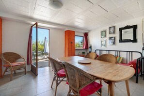 Spiseområde med et træbord og fletstole, en lille balkon med udsigt og en væg med billeder i rammer.