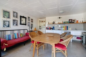 En hyggelig opholdsstue med spiseplads, en sofa med farverige puder og et køkken med moderne hårde hvidevarer.