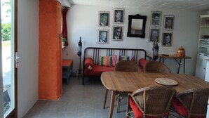 A dining area with a wooden table and wicker chairs, a red sofa, and a wall adorned with framed pictures. - Holiday Home 'Maison Cazac Marrakech' with Mountain View and Wi-Fi (Cazac)