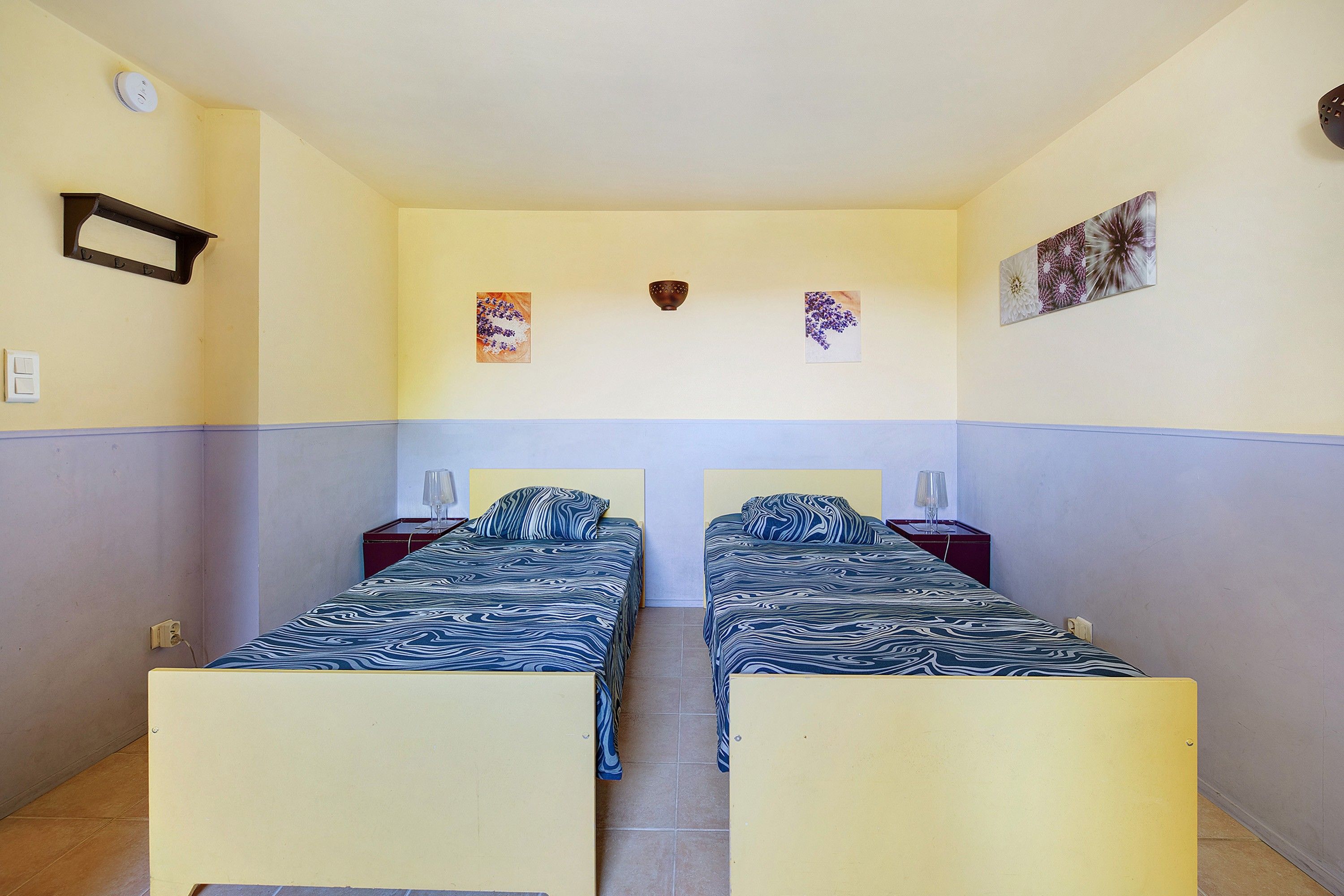 Una habitació amb dos llits, un llum penjada a la paret i dues fotografies a la paret.