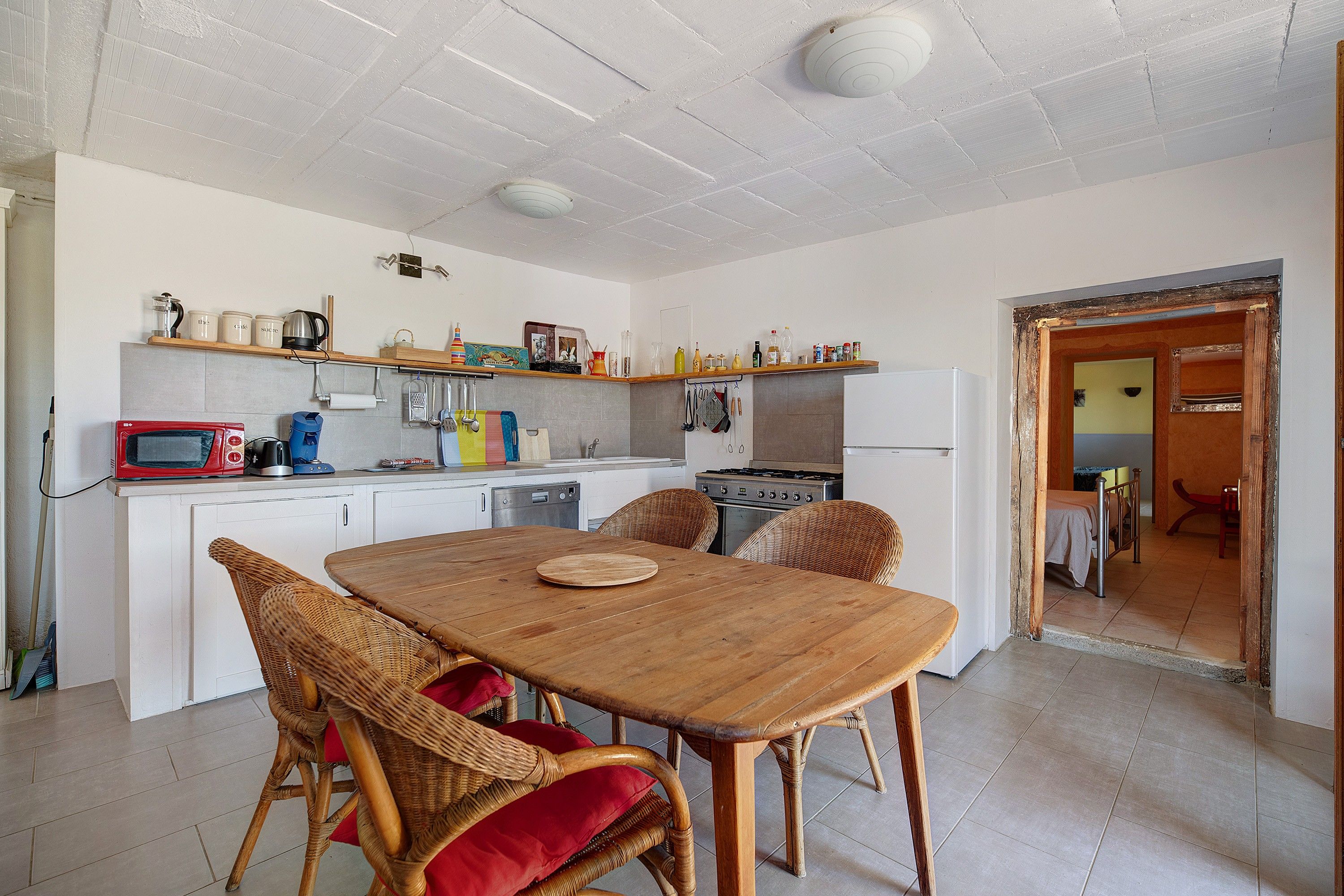 A kitchen with a dining table, wicker chairs, and various kitchen appliances.