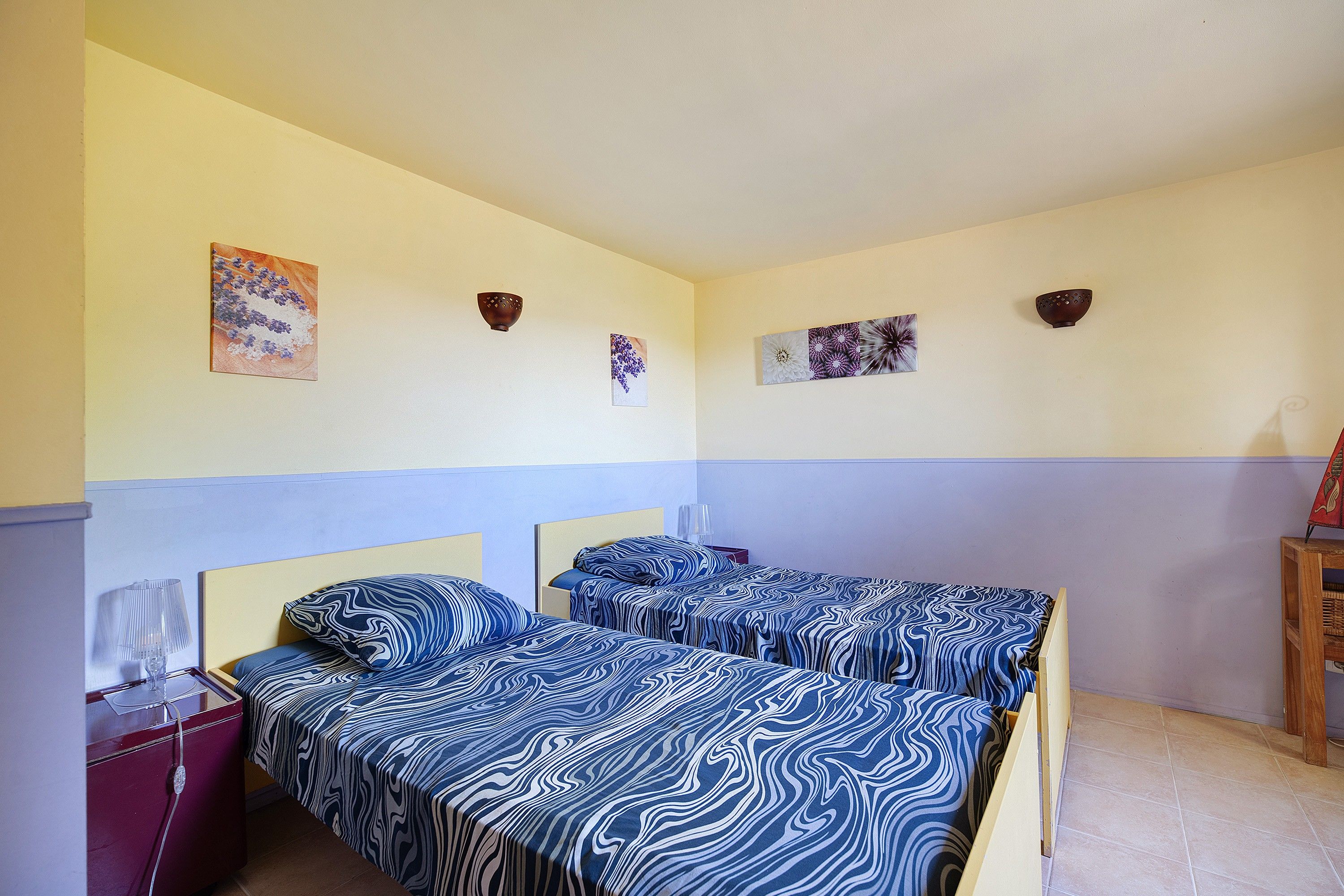 A room with two beds, a nightstand, and a small table with a lamp.