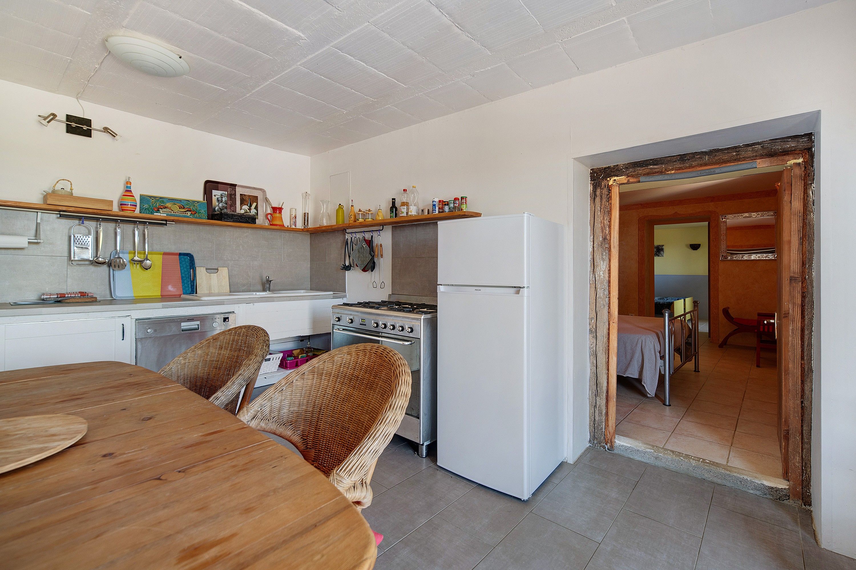 Une cuisine avec une table en bois, un fourneau, un réfrigérateur et un coin repas avec une chaise.