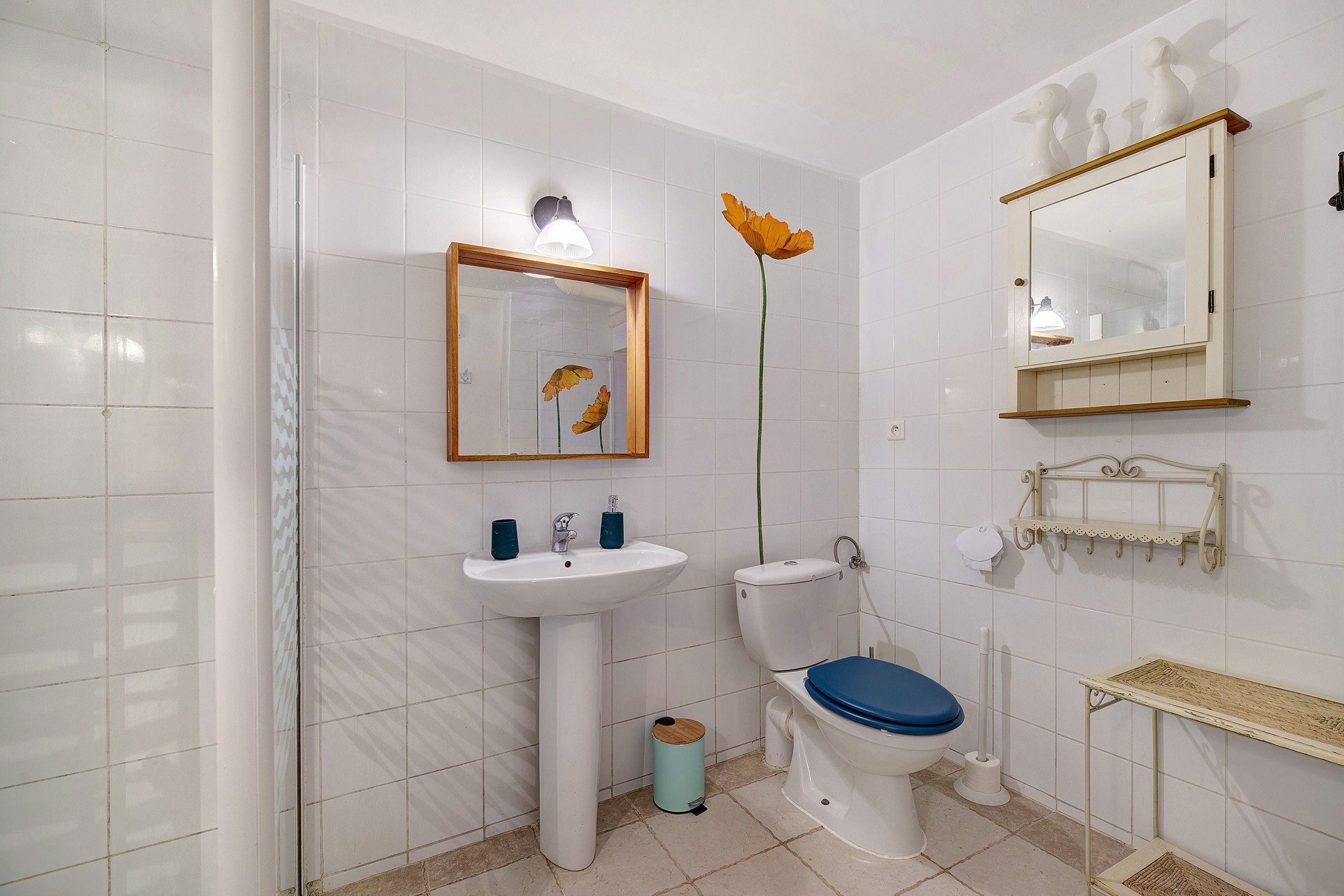 Une salle de bain avec un lavabo, des toilettes et un bidet, tous de couleur blanche. Un miroir est placé au-dessus du lavabo et un objet décoratif orne le mur.
