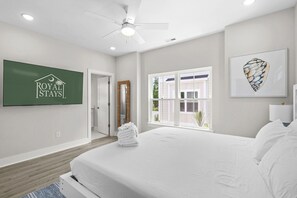A hotel room with a bed, a ceiling fan, a window with blinds, a wall-mounted TV displaying the hotel logo, and a framed artwork. - Blue Horizon 2 Blocks to Ocean Pets (North Myrtle Beach)