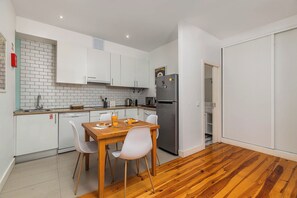 A compact kitchen with white cabinets, a stainless steel refrigerator, a wooden dining table with chairs, and a tiled backsplash. - Vintage-Chic Apartment in the City Center, Chiado (Lisboa)