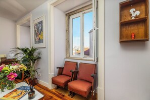 A room with two wooden chairs, a potted plant, a framed picture, and a window with a view of buildings. - Vintage-Chic Apartment in the City Center, Chiado (Lisboa)