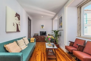 A living room with a teal sofa, a red armchair, a wooden coffee table, and a TV in the background. - Vrbo Property (Lisboa)