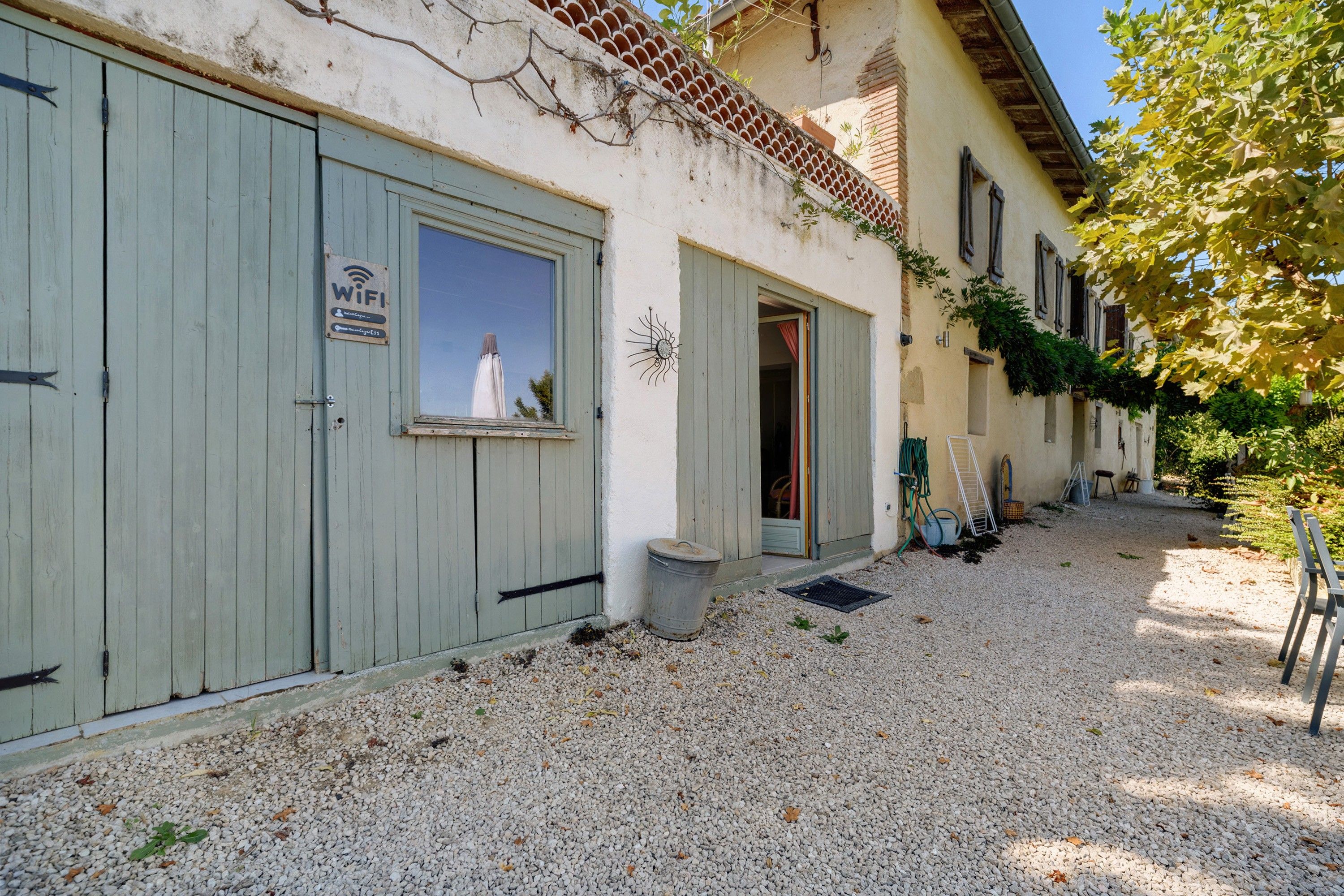 Un bâtiment avec des portes en bois fermées, un panneau indiquant la présence d’un réseau Wi-Fi et une allée gravillonnée.