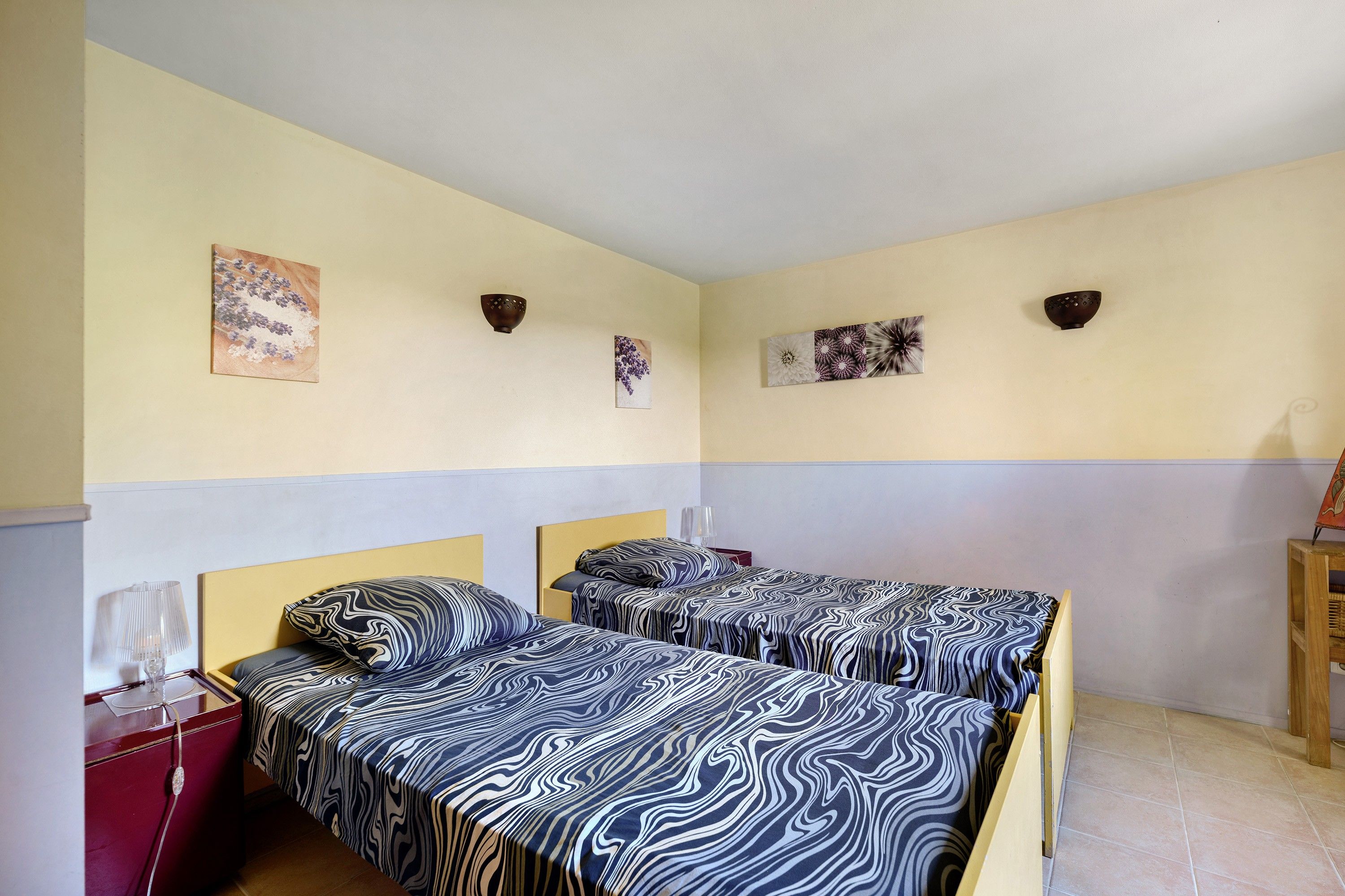 Une chambre avec deux lits, une table de chevet et des lampes fixées au mur.