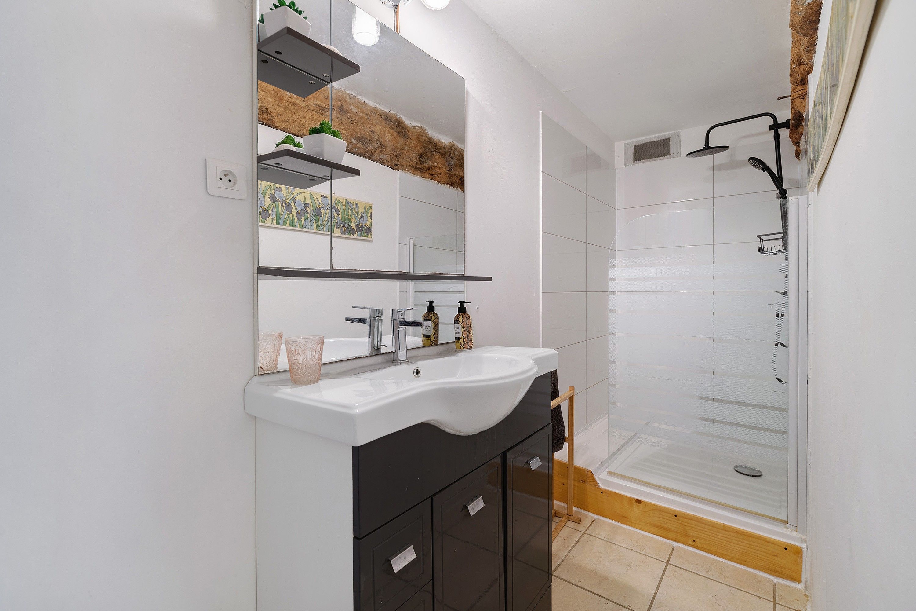 A modern bathroom with a white sink, dark cabinetry, a mirror, and a shower area.