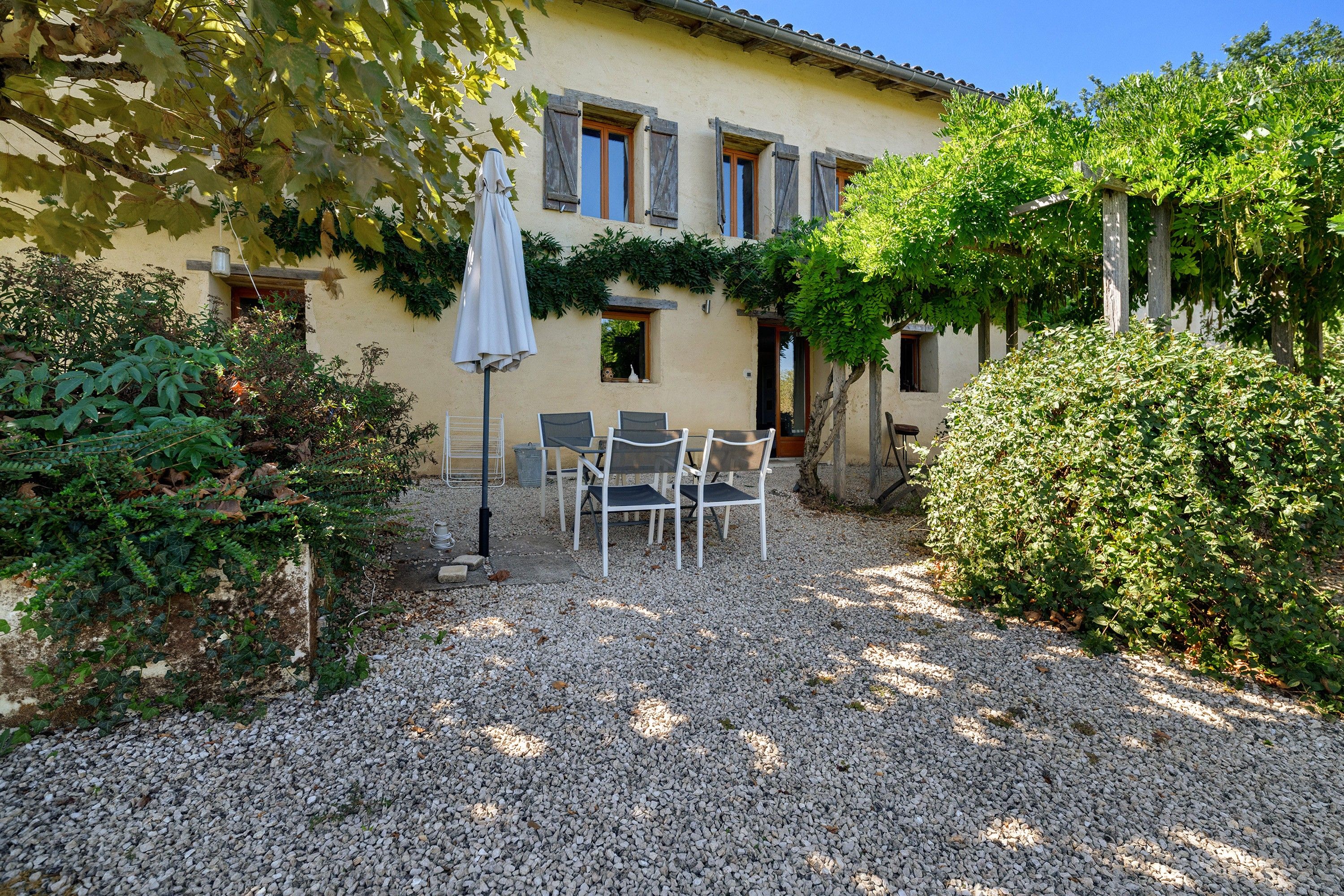 A patio with outdoor seating, a gravel ground, and a building with shutters.