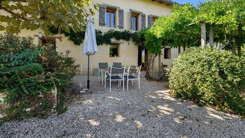 A patio with outdoor seating, a gravel ground, and a building with shutters.