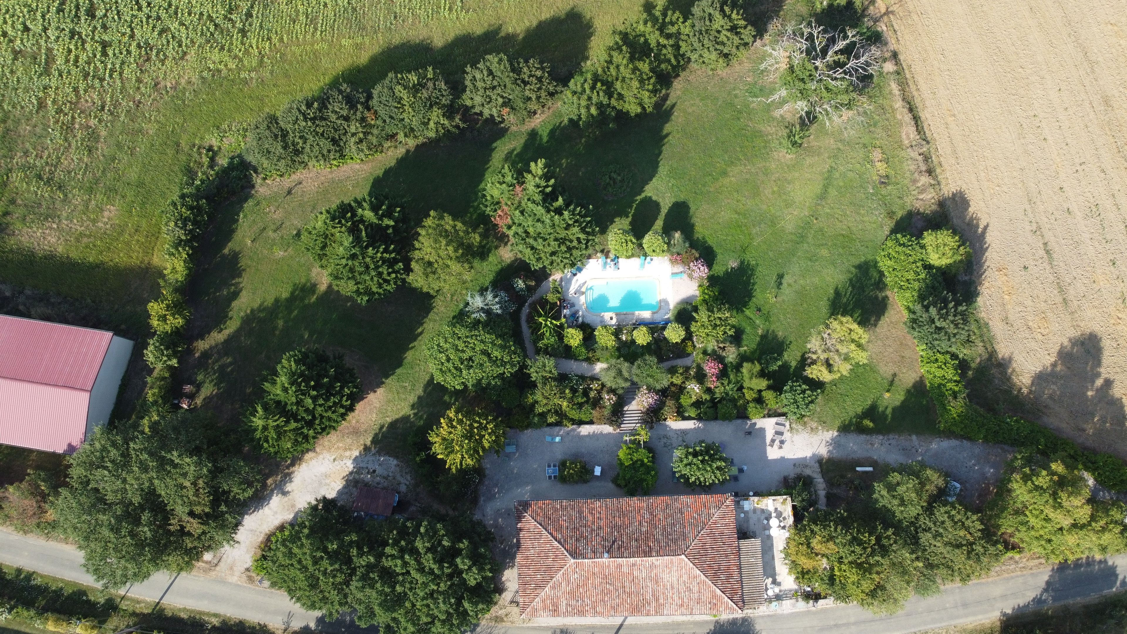 An aerial view of a property with a swimming pool, a red-roofed building, and a road.