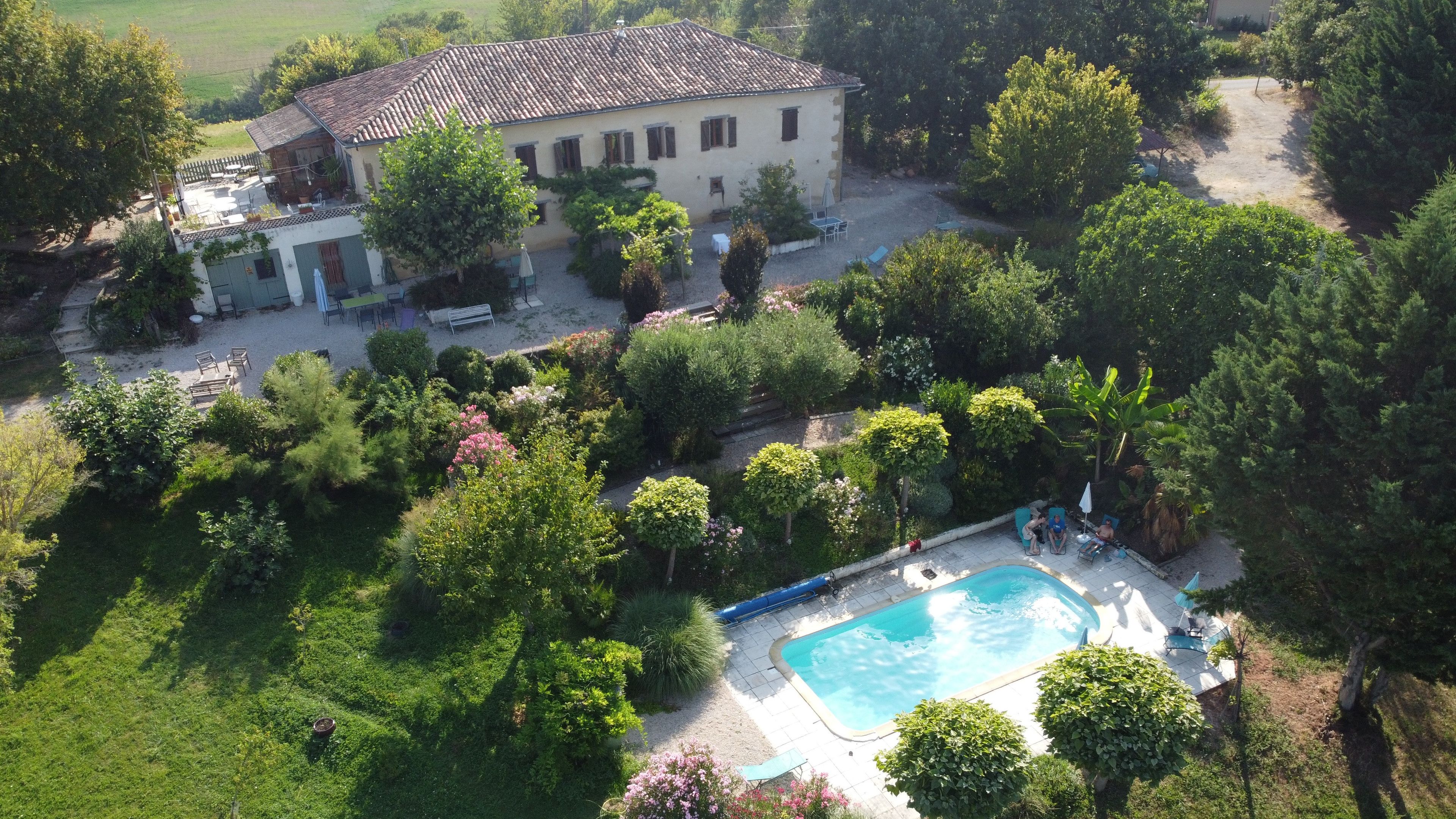 A residential property with a swimming pool, garden, and a large house with a tiled roof.
