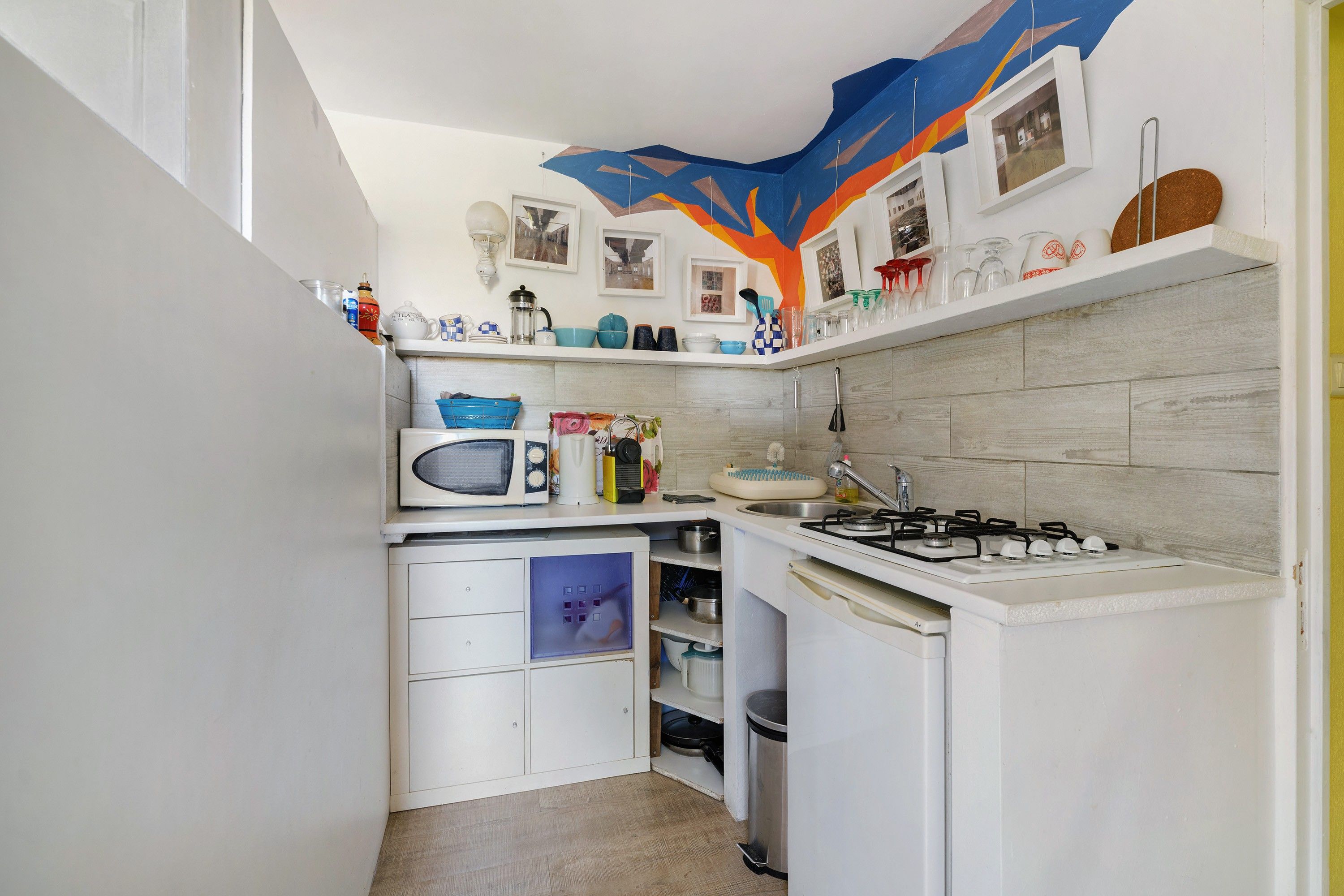 Une cuisine de taille réduite avec des meubles blancs, un four à micro-ondes, une cuisinière et un évier.