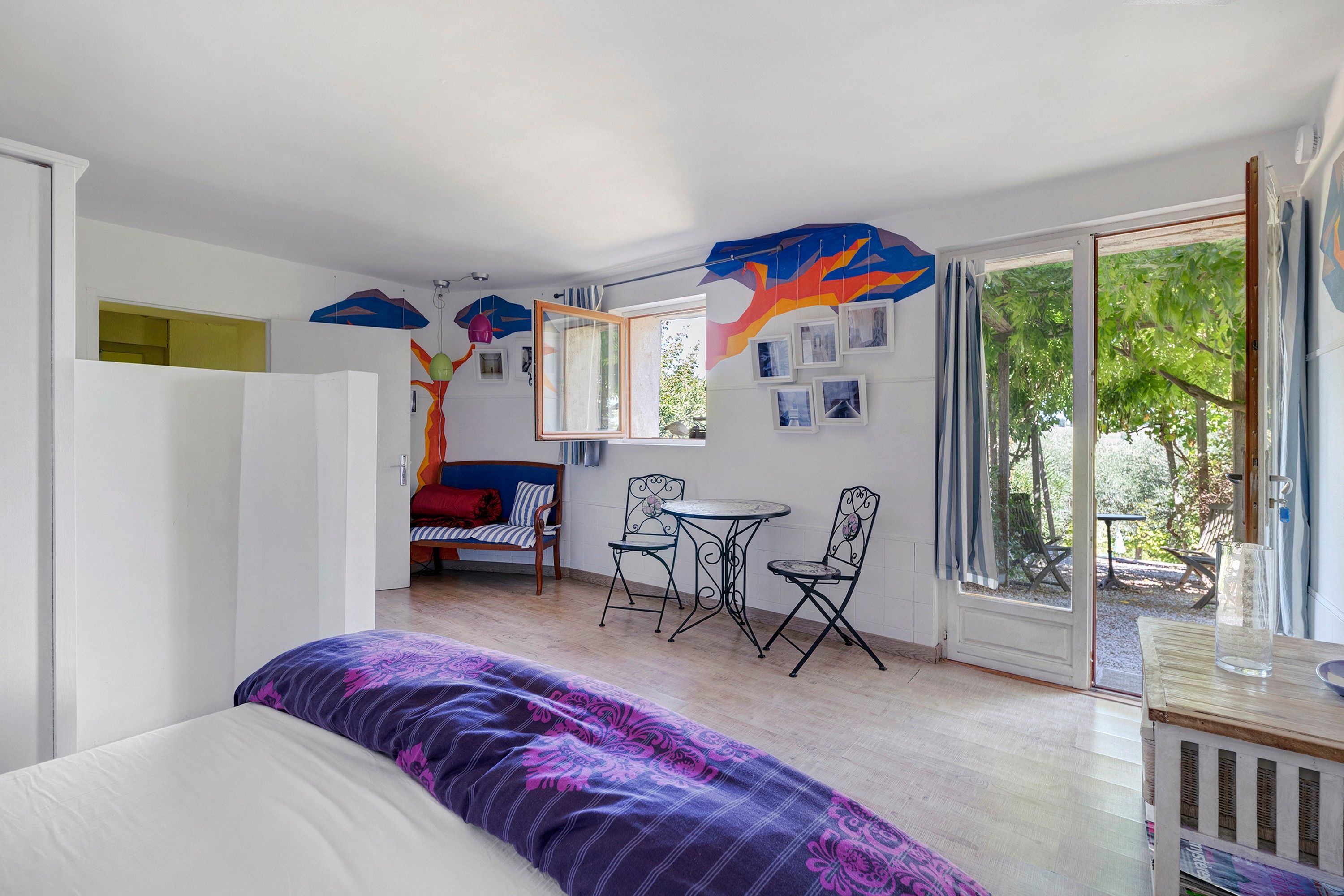 Een kamer met een bed, een eettafel met stoelen, een bank en een groot raam.