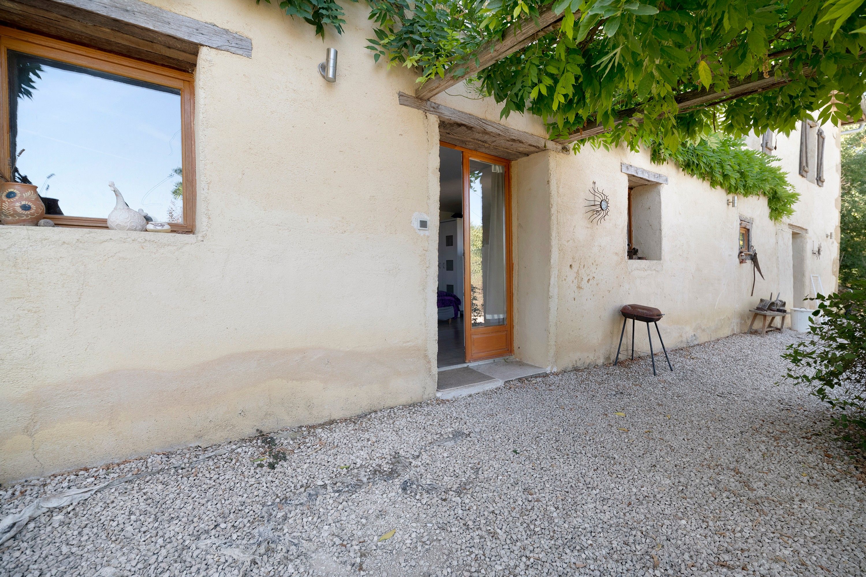 Un bâtiment rustique avec une allée en gravier, une porte en bois et un petit tabouret.