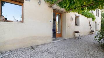 Un bâtiment rustique avec une allée en gravier, une porte en bois et un petit tabouret.