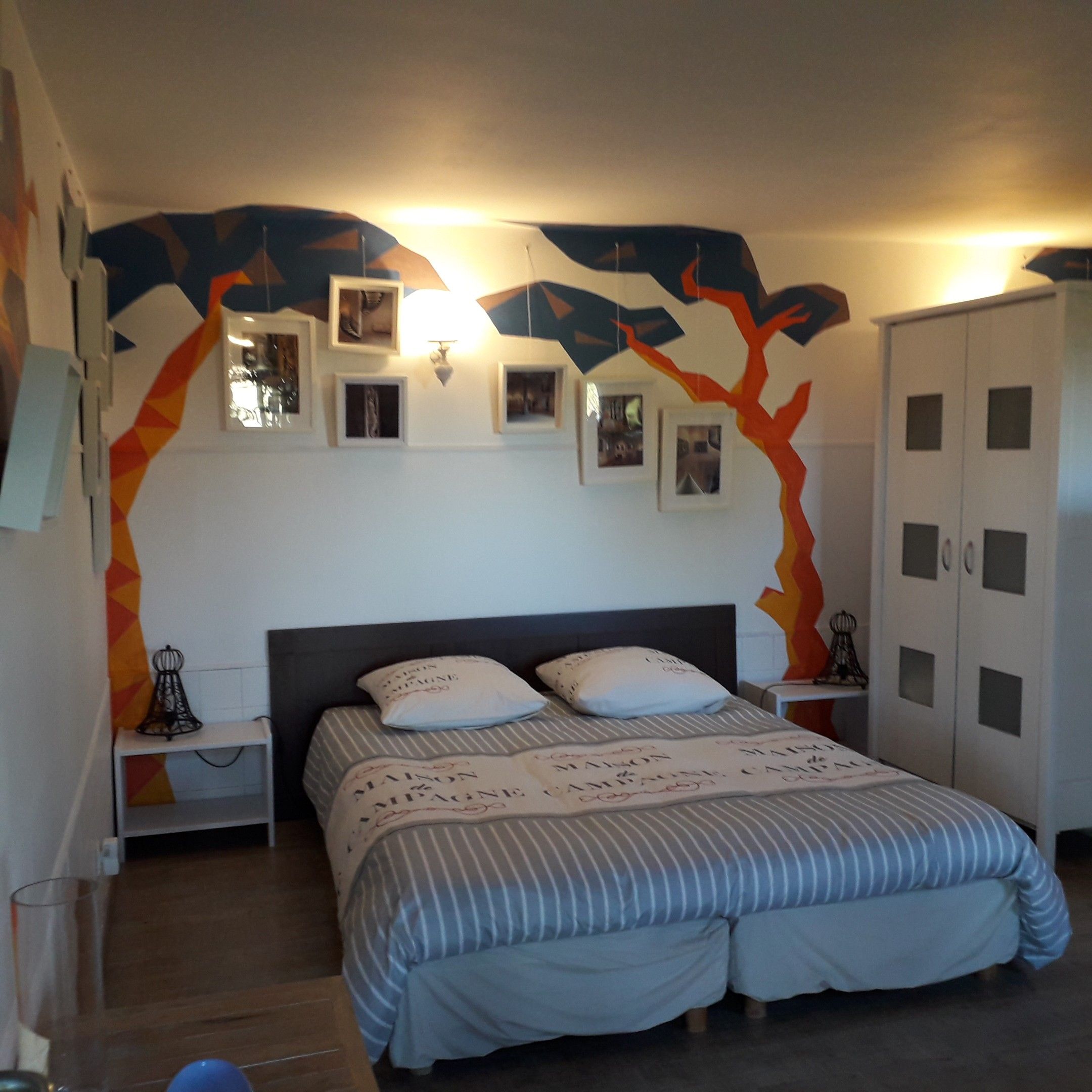 A bedroom with a bed, nightstands, a wardrobe, and wall-mounted picture frames.