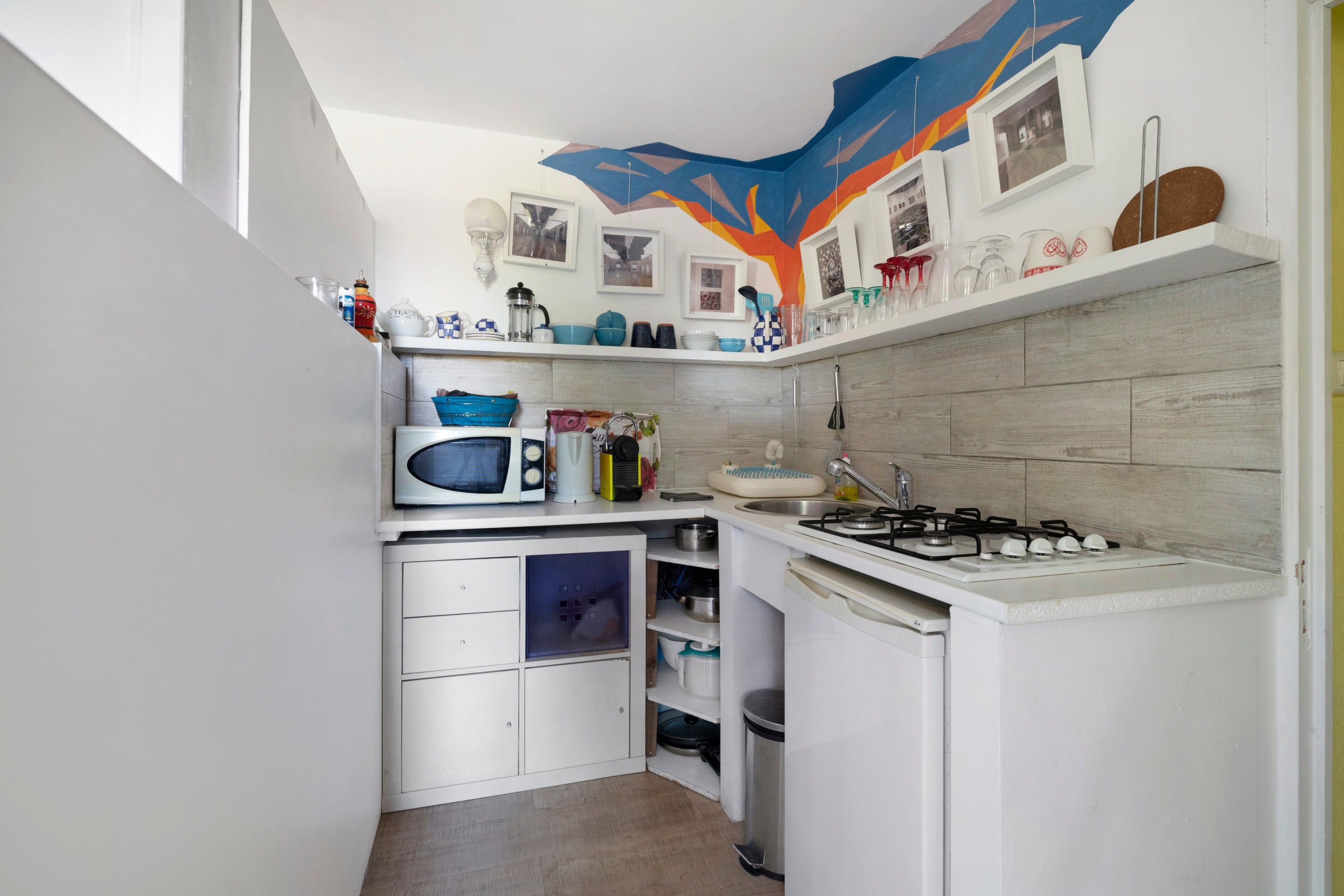 Een kleine keuken met witte keukenkastjes, een magnetron, een fornuis en diverse keukengerei.