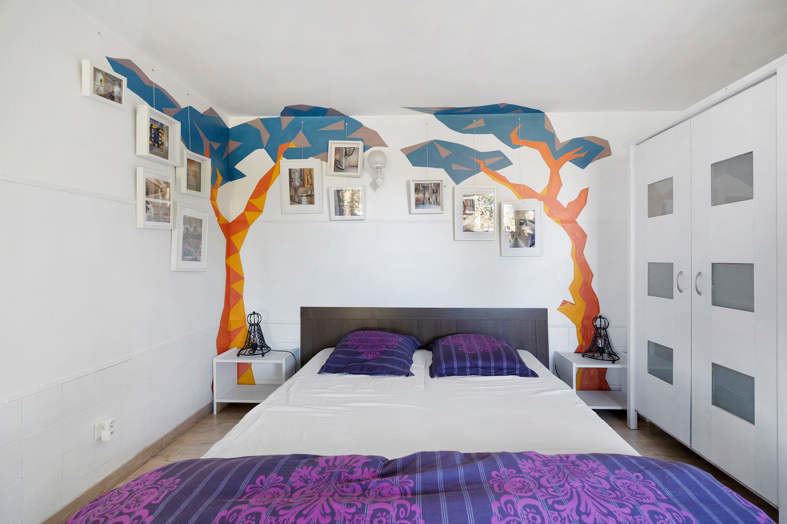 Une chambre à coucher comprenant un lit, des tables de chevet, une armoire et un mur orné de tableaux.