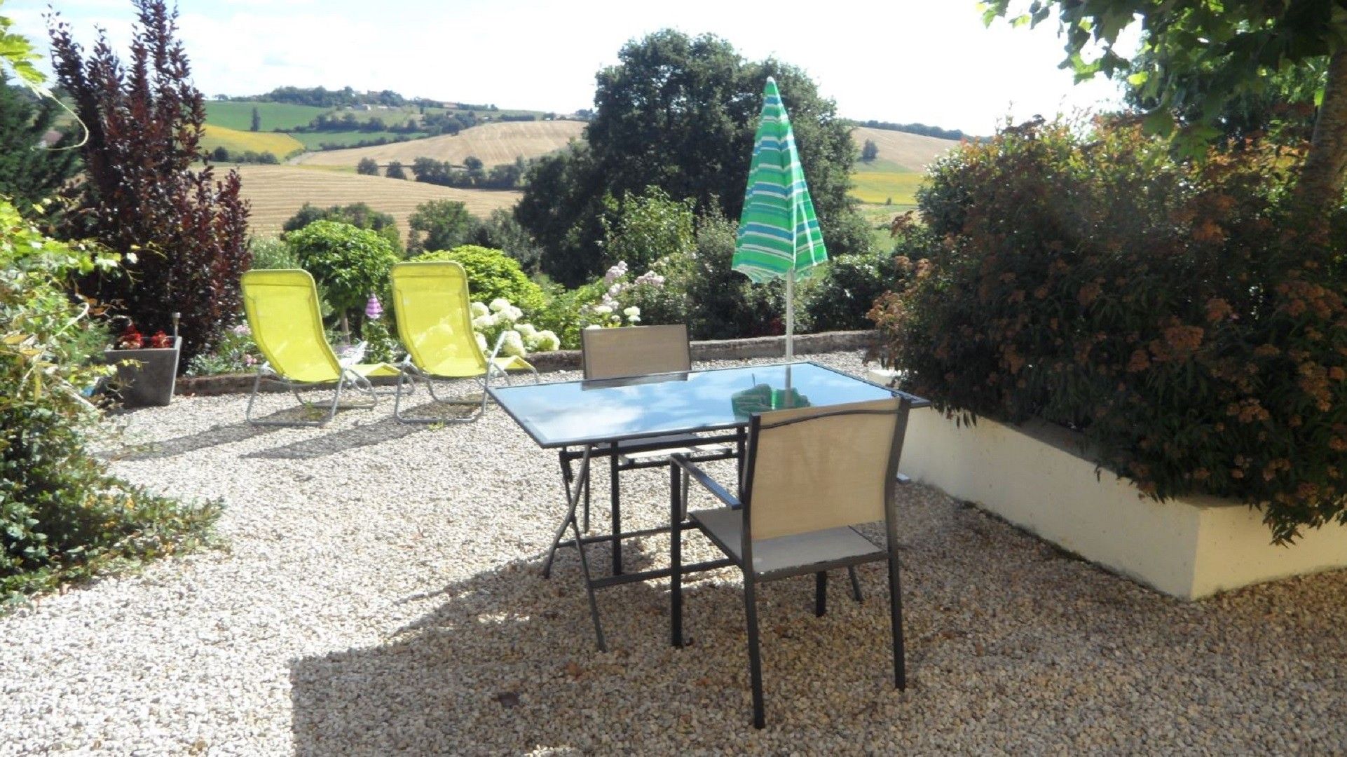 An outdoor patio with a table and chairs, surrounded by gravel and plants.