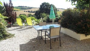 Une terrasse extérieure avec une table et des chaises, entourée de gravier et de plantes.