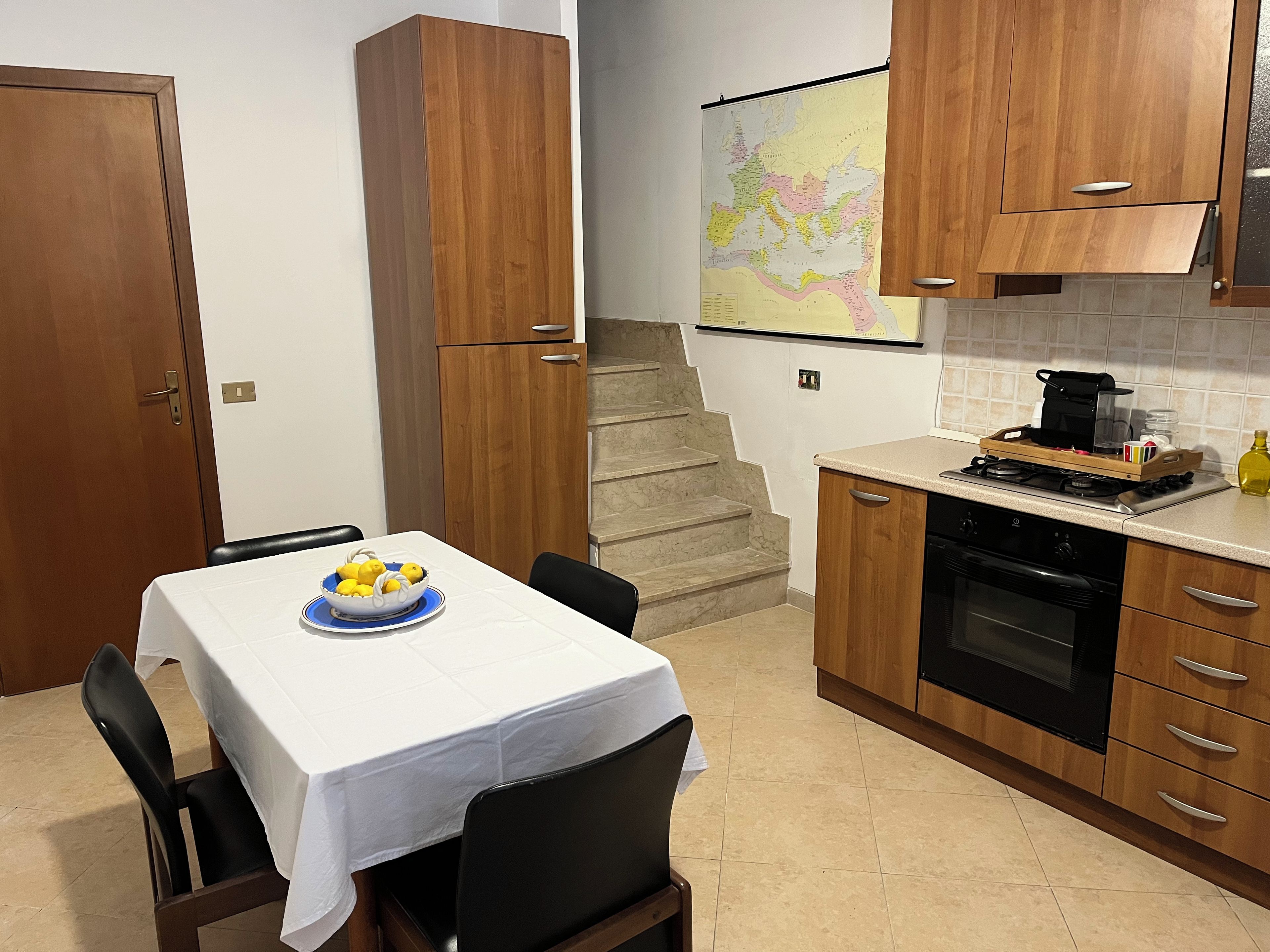 Una cucina con mobili in legno, un tavolo da pranzo con sedie, una mappa appesa al muro e un fornello.