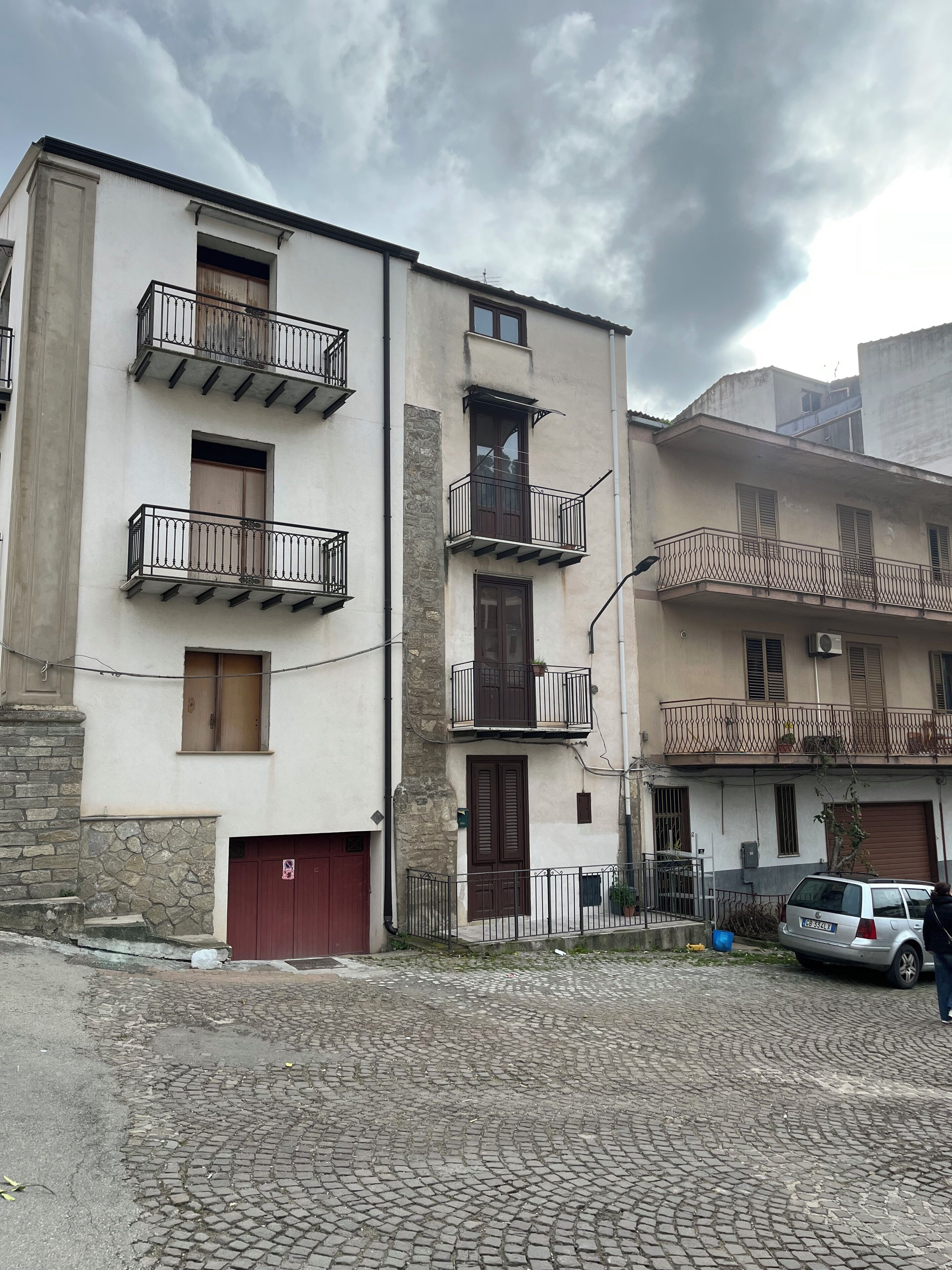 Un immeuble à plusieurs étages doté de balcons, d’une porte de garage rouge et situé dans une rue pavée.