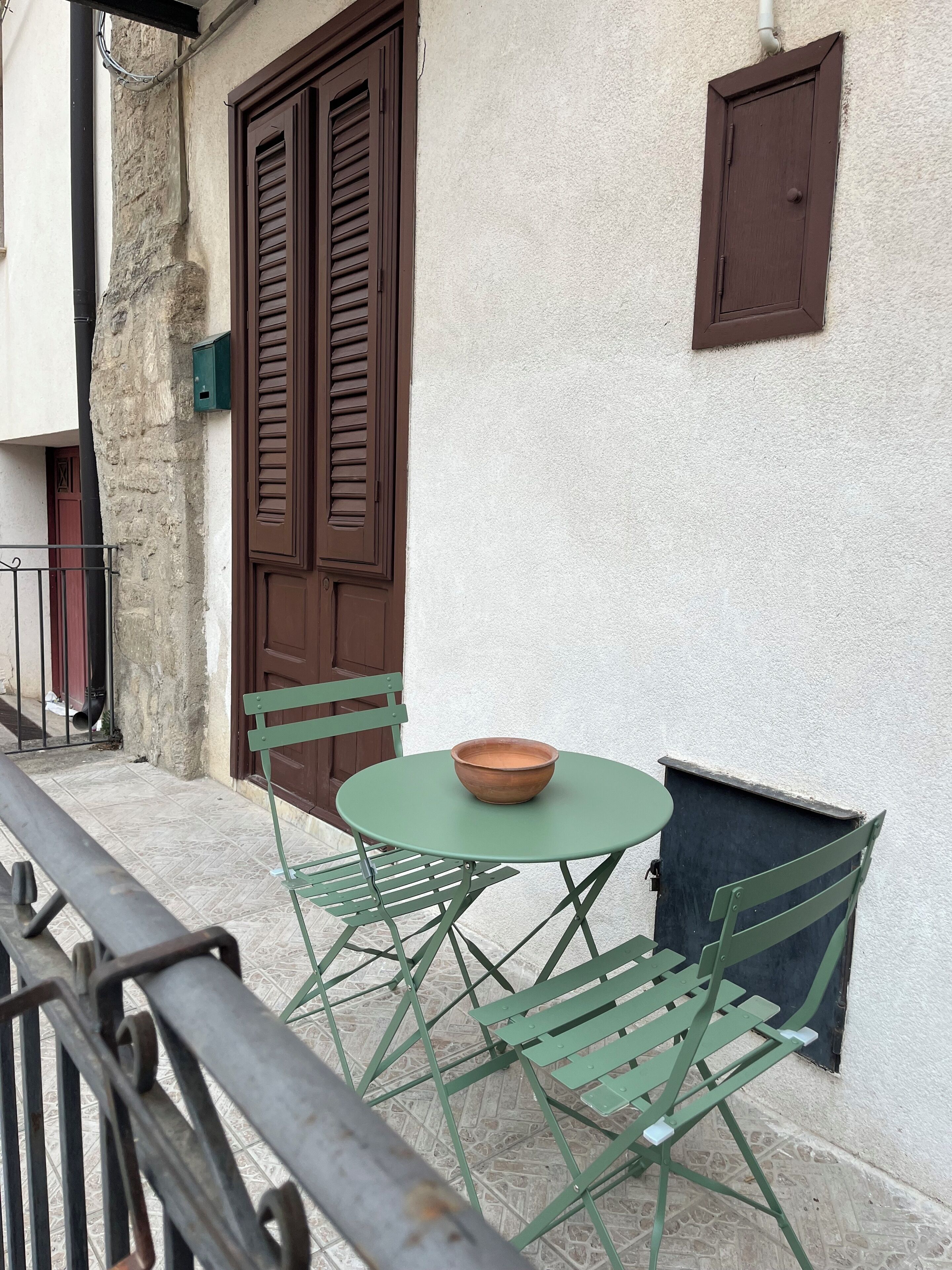 Un balcon avec une table et des chaises en métal vert, une porte marron et une petite fenêtre.