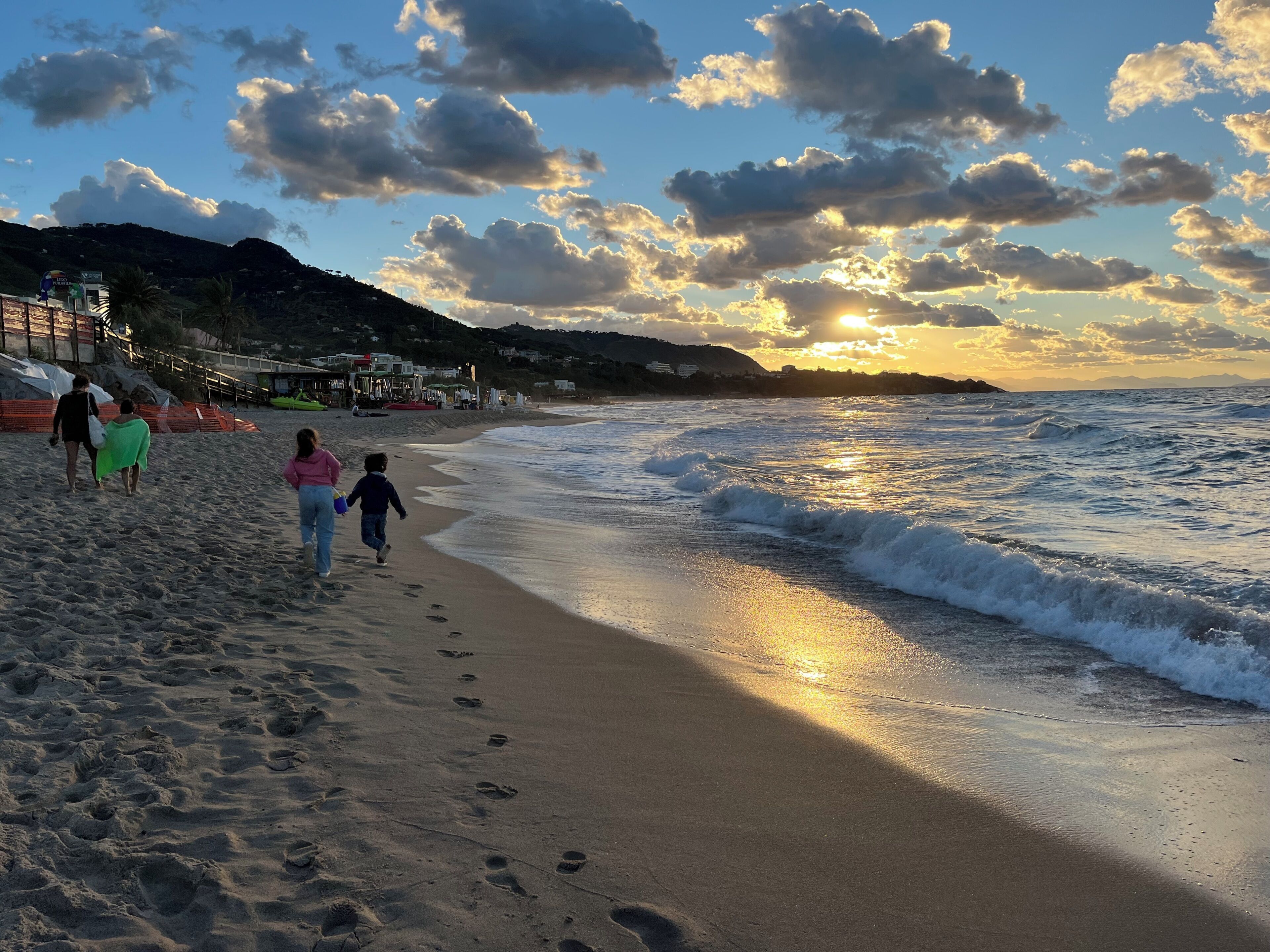Une plage où l’on voit des empreintes de pas menant à l’eau, un ciel dégagé et un coucher de soleil.