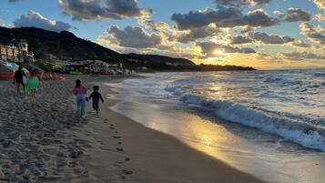 Une plage où l’on voit des empreintes de pas menant à l’eau, un ciel dégagé et un coucher de soleil.