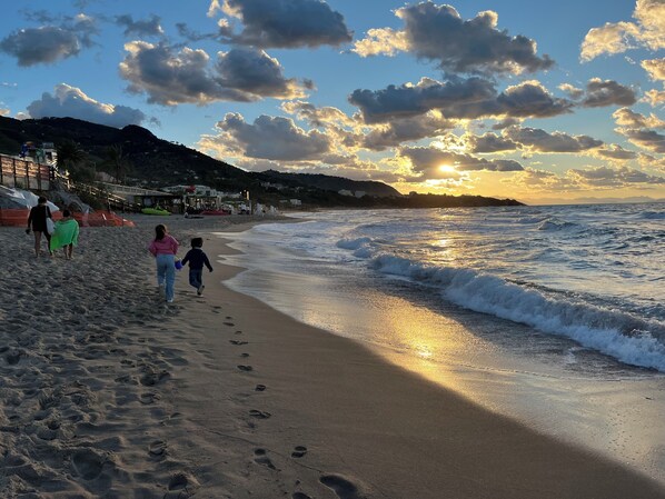 A beach with footprints leading to the water, a clear sky, and a sunset.