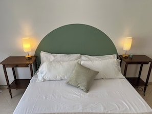 Een bed met witte beddengoed, een groen hoofdeinde en twee nachtkastjes met lampen.