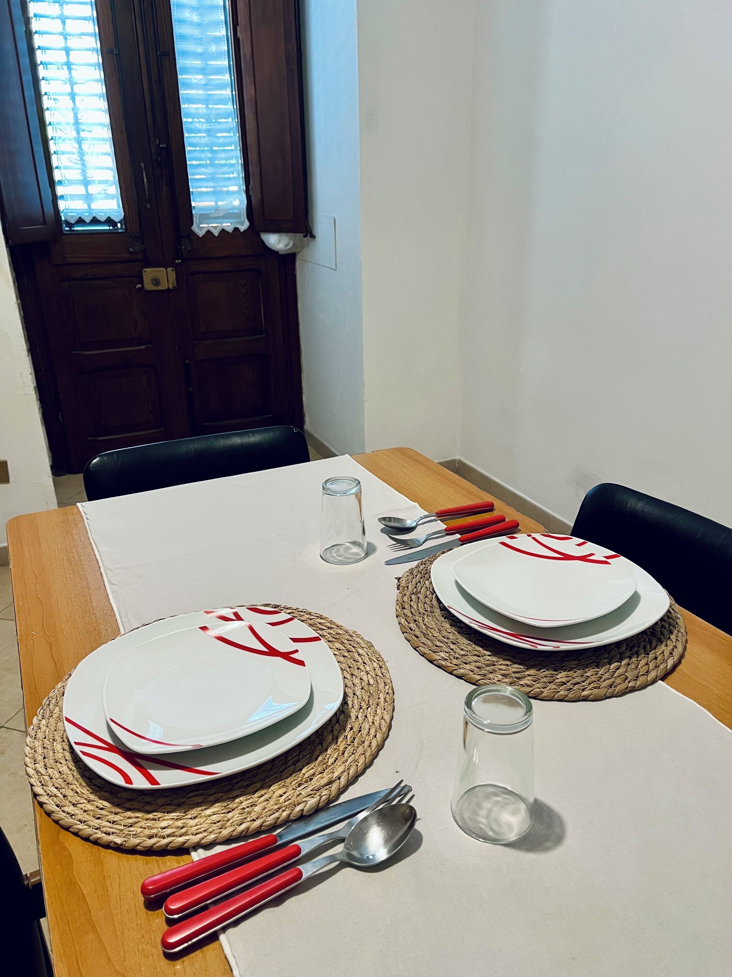 Une table à manger dressée avec des assiettes, des couverts et un verre.