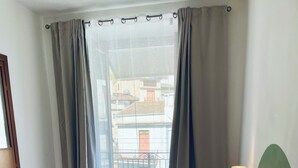 A hotel room with a bed, pillows, a bedside lamp, and a view of buildings through the window. - La Fontanella - Authentic Sicilan Retreat (Ciminna)