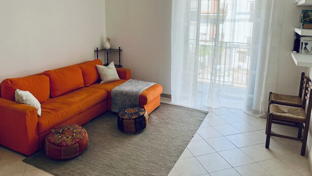 A living room with a sofa, ottomans, a rug, a chair, a table with a vase, and a window with curtains. - La Fontanella - Authentic Sicilan Retreat (Ciminna)