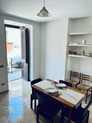 A dining area with a table set for two, chairs, a hanging light fixture, and a view through an open door to the outside. - La Fontanella - Authentic Sicilan Retreat (Ciminna)