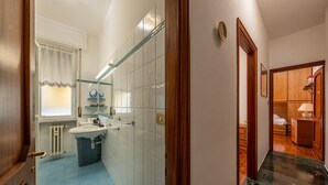 Casa de banho com lavatório, espelho e janela com cortinas.