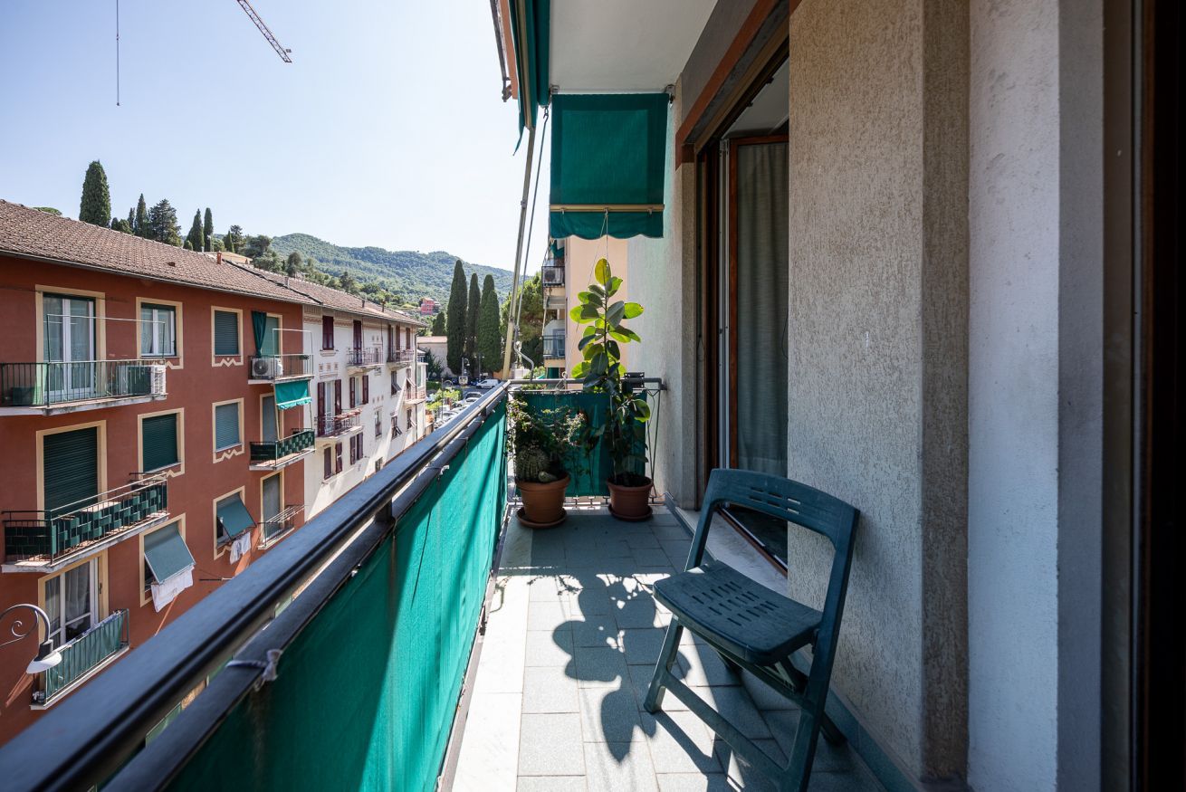 Ein Balkon mit einer Sitzbank, Blumentöpfen und Blick auf Gebäude und Hügel.
