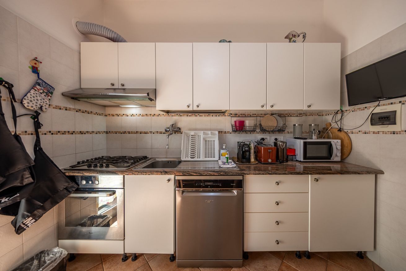 Une cuisine compacte avec des meubles blancs, un four encastré, un lave-vaisselle, un four à micro-ondes et une cuisinière à gaz.