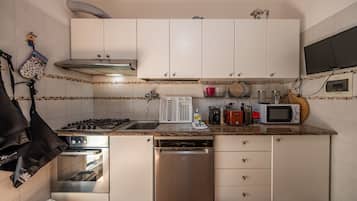 Une cuisine compacte avec des meubles blancs, un four encastré, un lave-vaisselle, un four à micro-ondes et une cuisinière à gaz.
