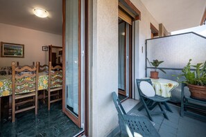 Een balkon met een tafel, stoelen, een potplant en een schuifdeur die leidt naar een binnenruimte met een eettafel en stoelen.