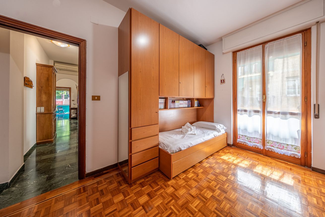 A bedroom with a wooden wardrobe, a bed, and a sliding glass door to a balcony.